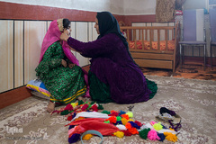 شوکت طاهری، ۴۶ساله و ساکن روستای یاسر شهرستان اندیکا است و با حمایت کمیته امداد امام خمینی(ره) به کار صنایع دستی مشغول است. شوکت طاهری در حال پوشاندن لباس محلی به نوه‌اش است که دوخت آن توسط خودش انجام شده.