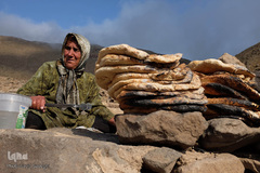 زن عشایر زیر آفتاب سوزان و گرمای تنور نان‌های محلی خود را آماده کرده است.