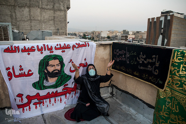 خانمی که با فاصله از دیگر عزاداران در حال دعا است.